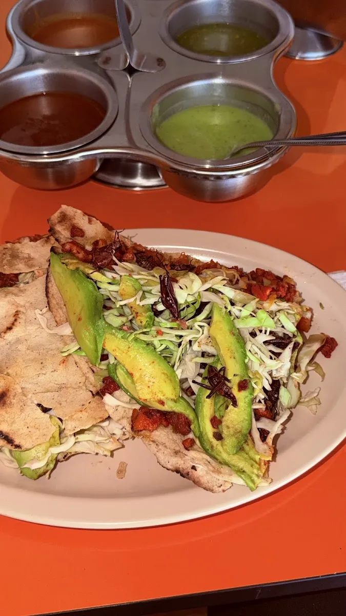 Tlayuda con col y aguacate junto a la charola de salsas