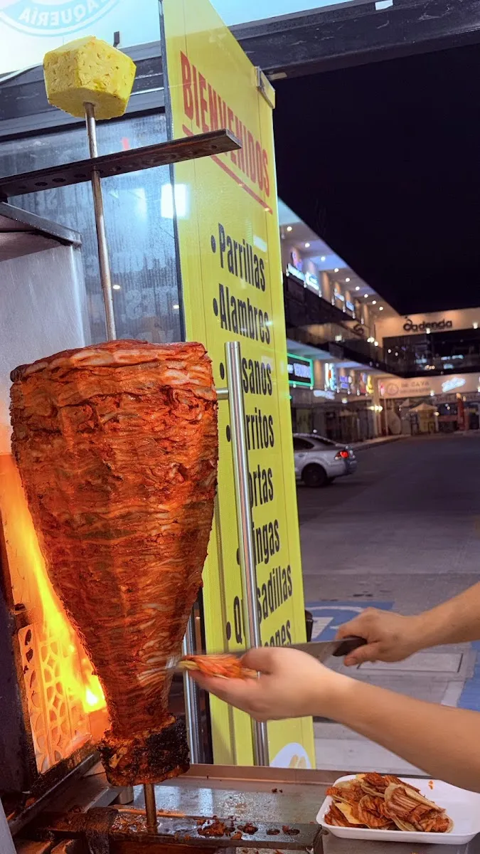 Trompo de pastor junto al letrero amarillo de la taquería, de noche