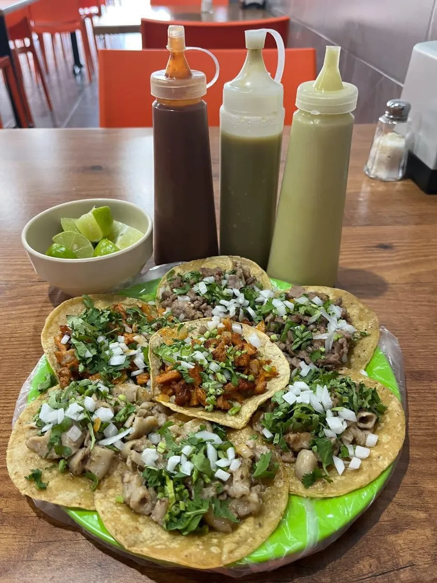 Tacos en un plato verde con salsas y limones